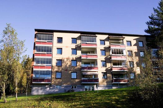 An apartment building in bright sunlight surrounded by green trees and grass