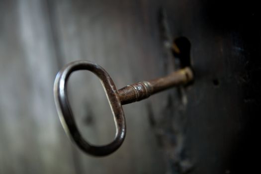 A skeleton key in a black door and lock.  Shallow depth of field.