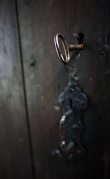 A skeleton key in a black door and lock.  Shallow depth of field.