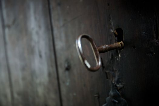 A skeleton key in a black door and lock.  Shallow depth of field with focus on key hole