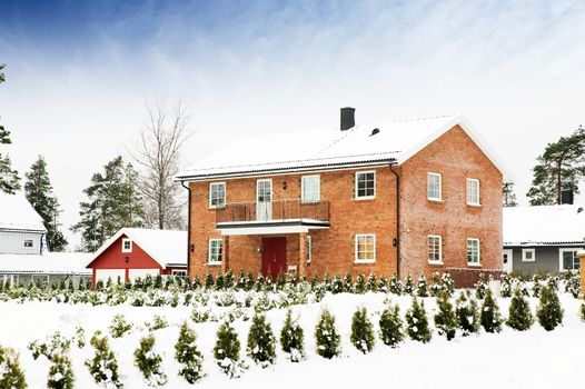 A large brick house in a nice neighborhood surrounded by bushes.