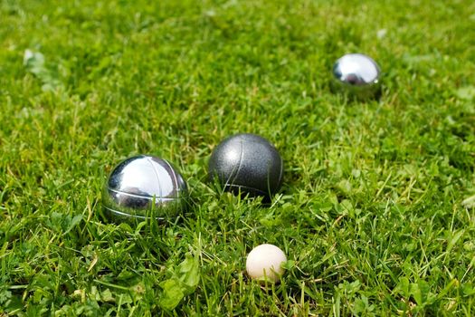 Bocce balls sitting in the green grass, close to the target. -shallow depth of field.-