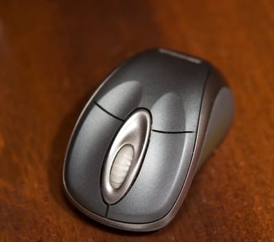 A close up detail of a grey cordless mouse on a wodden table.