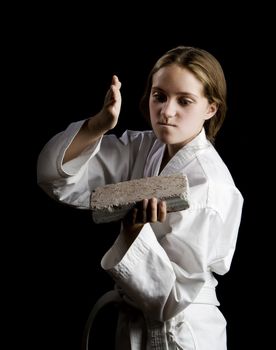 Young girl karate chopping a brick on black background