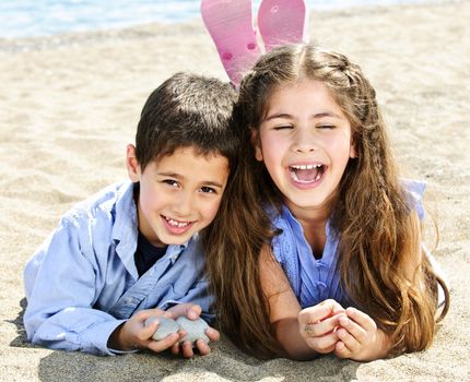 Portrait of brother and sister laying on sand at the beach