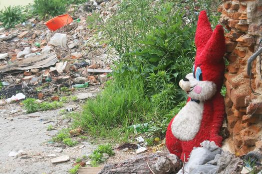 Giant red stuffed bunny in garbage filled deserted city lot