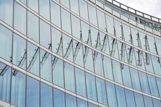 A modern office building facade made of steel and glass is reflecting a crane