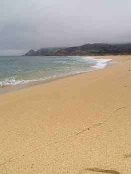 Shoreline covered in fog and mist, with mountains in the background.