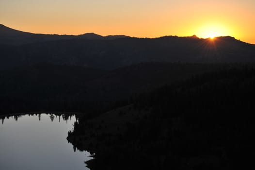 Darkness still keeps the mountains in shadow until the sun rises while the lake mirrors the surrounding trees.