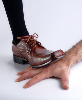 Shoe of a businessman showing his power by crushing the hand of another man