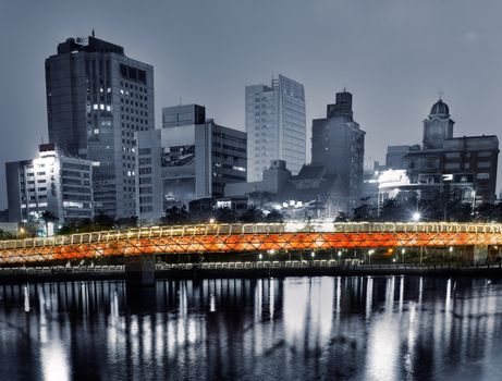 Cityscape of apartments with river and bridge in night.