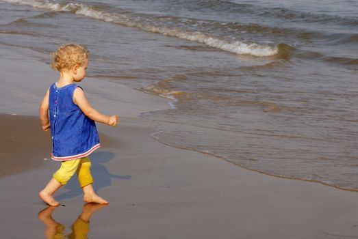 Little girl dressed walking steady toward the shore, ready to try the water 