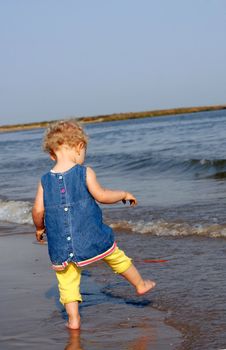 Little girl dressed at the seashore ready to try the water with one foot