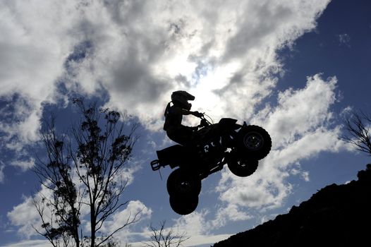 A silhouette of a quad bike (ATV) jumping through a cloudy sky