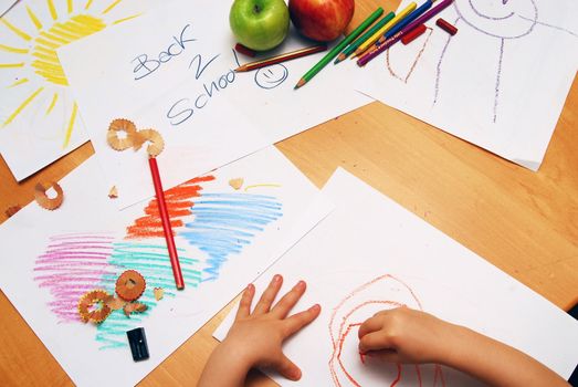 Little hands drawing between school supplies and apples