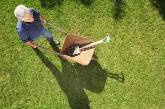 A gardener setting off to work with his wheelbarrow and tools, taken from a high viewpoint. Space for text to right and at base of image