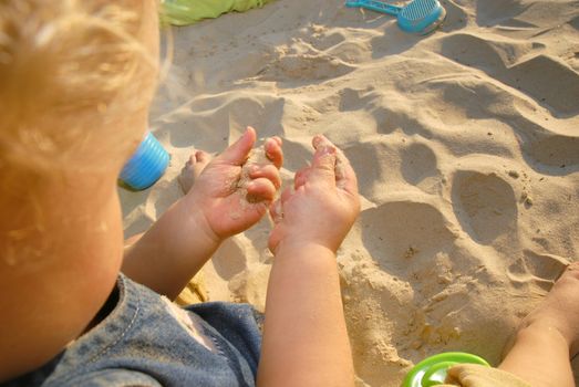 Baby girl playing on the beach with sand in her hands and plastic toys. Upper view