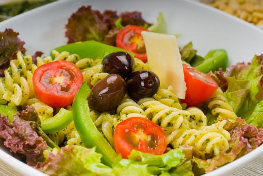 fresh healthy homemade italian fusilli pasta salad with parmesan cheese,pachino cherry tomatoes, black olives and mix vegetables ,dressed with extra-virgin olive oil and pesto sauce