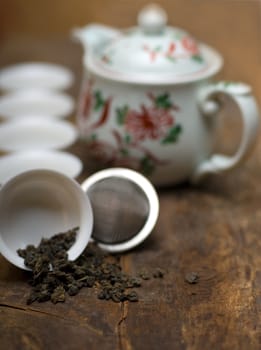 dry green chinese tea set,with strainer closeup,cups and teapot on background over old wood board