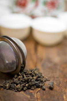 dry green chinese tea set,with strainer closeup,cups and teapot on background over old wood board