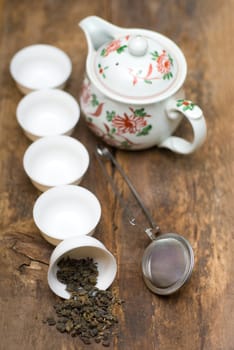 dry green chinese tea set,with strainer closeup,cups and teapot on background over old wood board