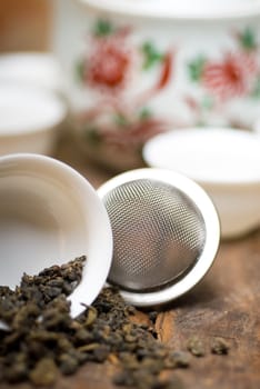 dry green chinese tea set,with strainer closeup,cups and teapot on background over old wood board