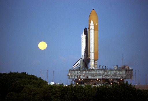 Shortly before dawn, a red-rimmed moon helps to light the way for the Space Shuttle Atlantis as it rolls out to Launch Pad 39A in preparation for launch of Mission STS-86. STS-86 will be the seventh docking of the Space Shuttle with the Russian Space Station Mir. Liftoff is targeted for no earlier than September 22. Photo taken: 08/18/1997. ** Credit: NASA / yaymicro.com **