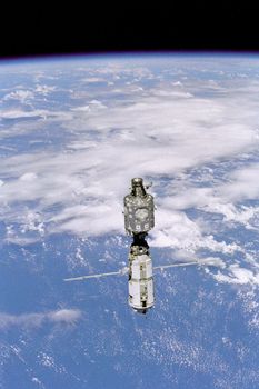 Backdropped against white clouds and blue ocean waters, the International Space Station (ISS) moves away from the Space Shuttle Discovery. The U.S.- built Unity node (top) and the Russian-built Zarya or FGB module (with the solar array panels deployed) were joined during a December 1998 mission. ** Credit: NASA / yaymicro.com **