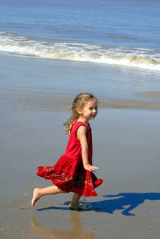 Happy girl on the beach, in a red beautiful dress, running towards the seashore
