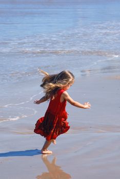 Happy girl on the beach, in a red beautiful dress, playing at the seashore