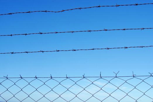 Cut wire fence with clear blue sky background.
