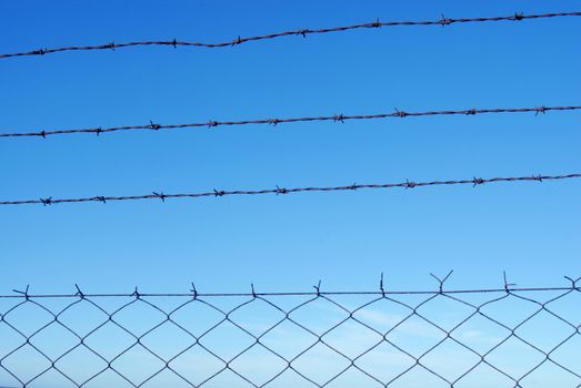 Cut wire fence with clear blue sky background.