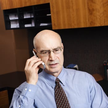 Caucasian middle-aged businessman sitting in office talking on cellphone.