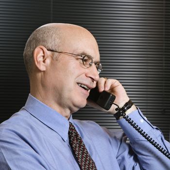 Caucasian middle-aged businessman smiling and talking on telephone.