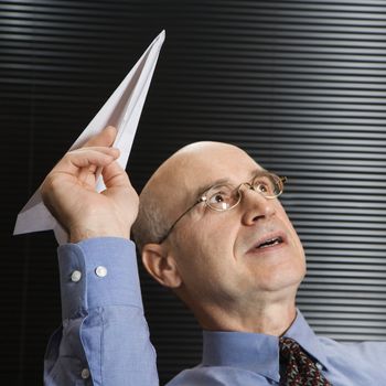 Caucasian middle-aged businessman playing with paper airplane.