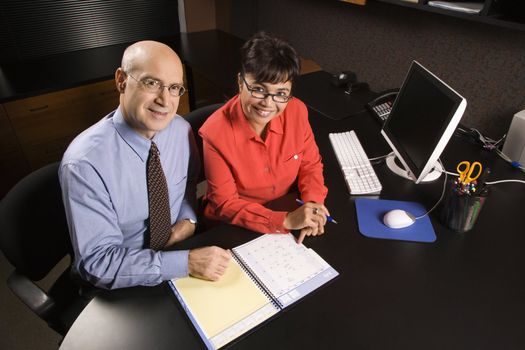 Businessman and businesswoman in office smiling going over appointment calendar.