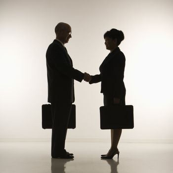 Caucasian middle-aged businessman and Filipino businesswoman standing looking at eachother shaking hands against white background.