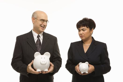 Caucasian middle-aged businessman and Filipino businesswoman holding different sized piggybanks.