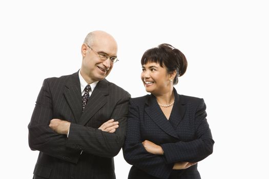 Caucasian middle-aged businessman and Filipino businesswoman standing with arms crossed against white background smiling at eachother.