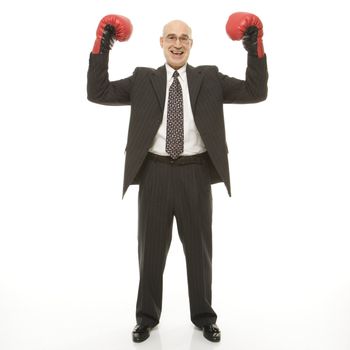 Smiling Caucasian middle-aged businessman standing with arms raised wearing boxing gloves.