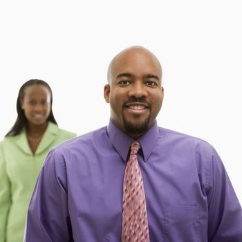 African-American businessman looking at viewer and smiling with businesswoman in background.