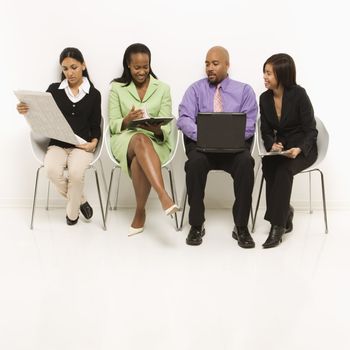 Multi-ethnic business group of men and women sitting looking at laptop and papers.