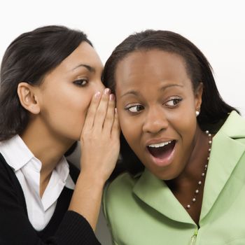 Indian young adult woman whispering in ear of mid-adult African-American woman.