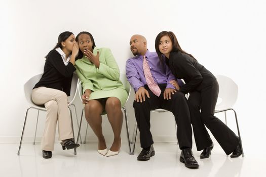 Multi-ethnic businesswomen whispering and making faces while colleagues eavesdrop.