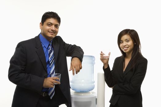 Vietnamese businesswoman and Indian standing at water cooler looking at viewer.