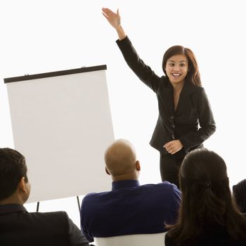Vietnamese mid-adult woman standing in front of business group gesturing for a presentation.