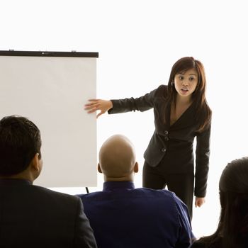 Vietnamese mid-adult woman standing in front of business group pointing to presentation.