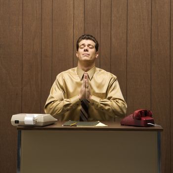 Caucasion mid-adult retro businessman sitting at desk praying in gratitude.