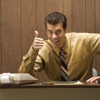 Caucasion mid-adult retro businessman sitting at desk giving overenthusiastic thumbs up.