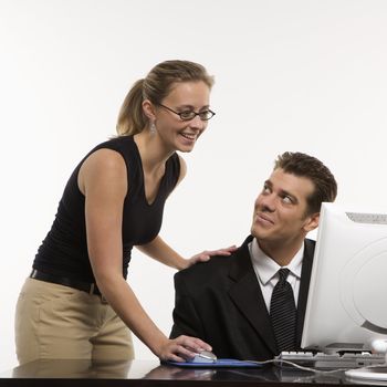 Caucasian mid-adult woman touching mid-adult man's shoulder and using mouse at computer.